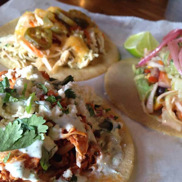 Close-up of three open face chicken tacos with cilantro, sour cream, jalapenos and pickled onions
