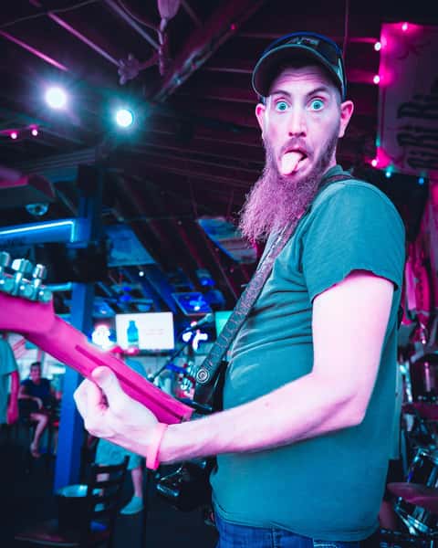A lively musician with a long beard and baseball cap enthusiastically playing a guitar on stage at Captain Archie's in Myrtle Beach.