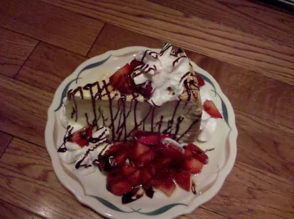 slice of cheesecake with whipped cream, strawberries and chocolate syrup