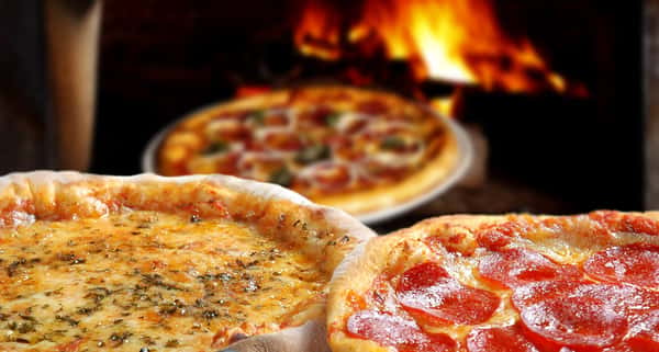 cheese pizza, pepperoni pizza and a vegetable pizza showcased in front of a brick oven