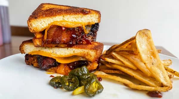 Grilled cheese sandwich with melted cheese, glazed brisket, pickled jalapeños, and a pile of steak fries.