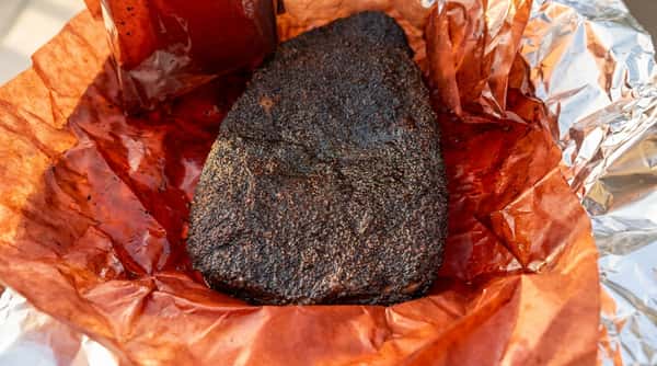 Smoked brisket with a dark, textured bark, wrapped in red butcher paper.