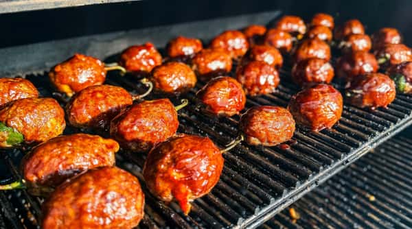 Pork belly burnt ends on a smoker grill with a glistening, reddish-brown glaze.