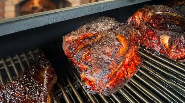 Two large pieces of dark brown, crusted meat cooking on a metal grill.