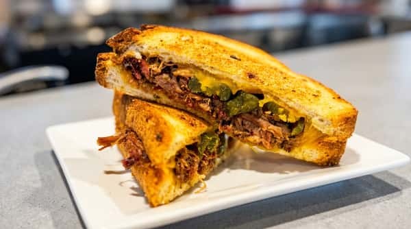 Grilled cheese sandwich stuffed with shredded meat, melted yellow cheese, and dark green peppers, cut in half and stacked on a white plate.