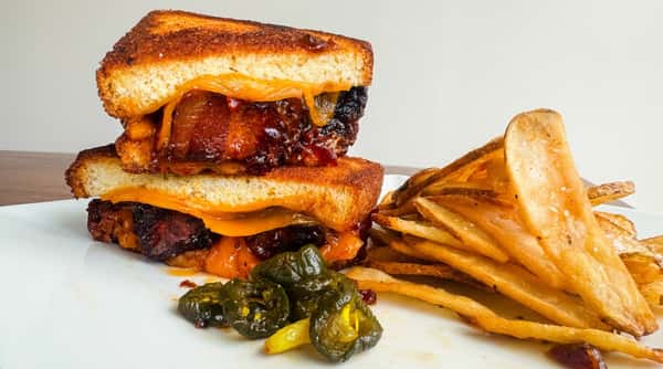BBQ brisket sandwich with melted cheese and pickled jalapeños, served with a side of fries.