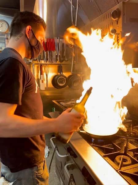 staff member in kitchen with flames coming from stove