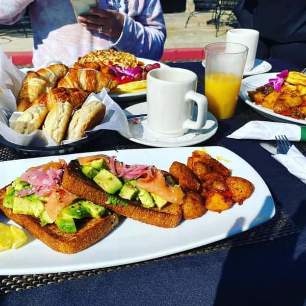 avocado toast with glass of ornage juice, croissant, and other breakfast items