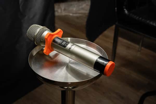 Wireless microphone with silver body, orange windscreen, and black accents resting on a round metallic stand.