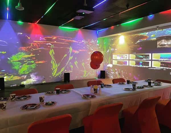 Long table set for a party with wall projections of an underwater scene and colorful lights.