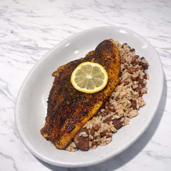 Blackened fish fillet topped with a lemon slice over dirty rice