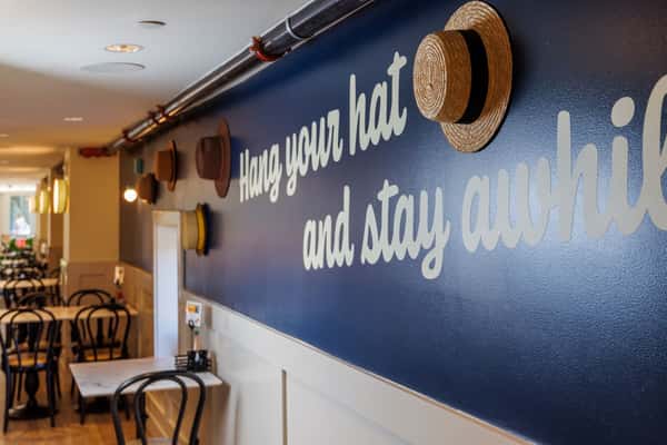 Dining room with a navy accent wall that reads "Hang your hat and stay awhile" and hats on display