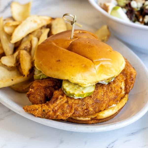 Fried chicken sandwich with pickles and slaw on a toasted bun, served with fries