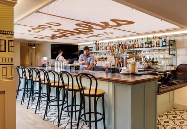 Bar counter with stools, a bartender, and a patterned ceiling
