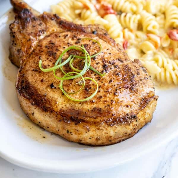 Grilled pork chop garnished with green onions, served with pasta salad