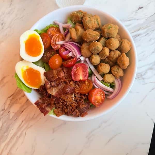 Salad bowl with soft-boiled eggs, tomatoes, bacon, red onion, and crispy croutons