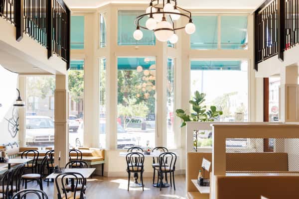 Bright dining room with tall windows, a chandelier, and bistro tables and chairs
