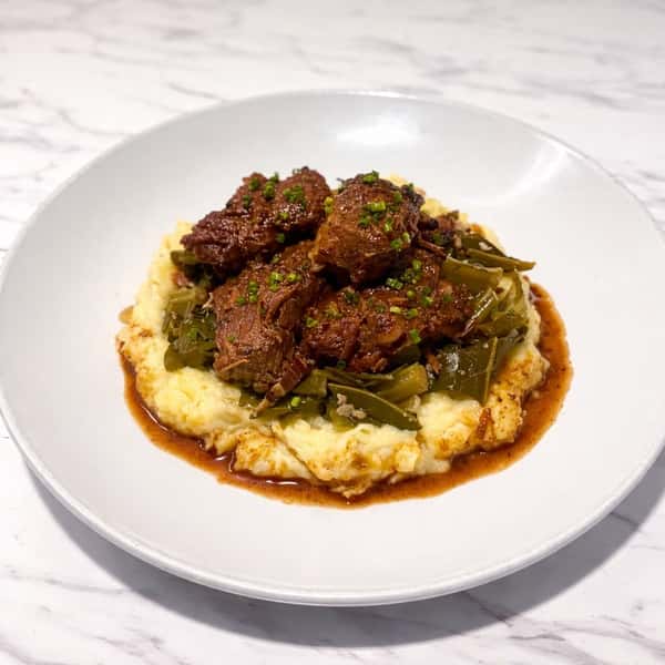 Braised meat with sautéed greens over creamy grits in a savory pan sauce