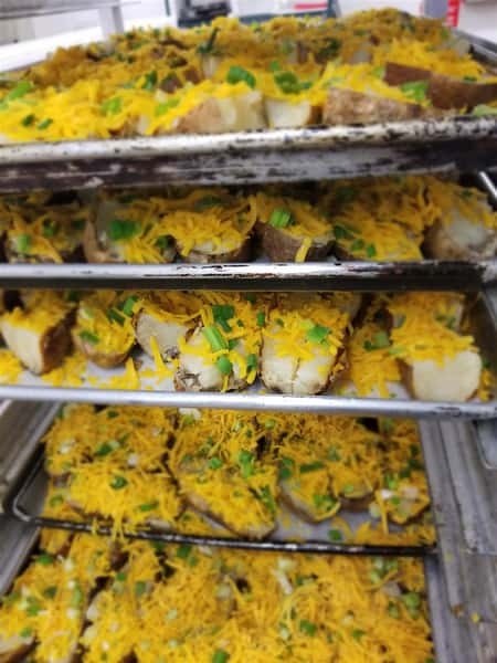 An assortment of Baked Potatoes topped with cheese on multiple trays