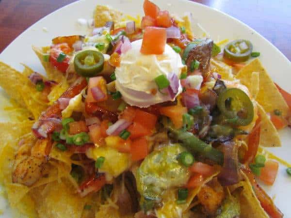Spicy Chicken Nachos - A generous portion of hand cut tortilla chips, topped with thinly sliced BBQ chicken, applewood smoked bacon, sliced jalapenos, diced tomatoes, scallions and shredded cheddar and Monterey jack.