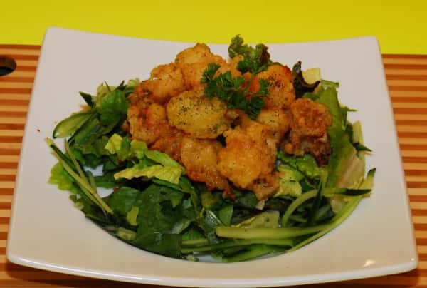A shrimp tempura salad is placed over lettuce and cucumber with a parsley garnish.