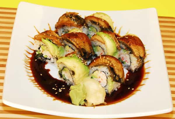 Sushi rolls topped with eel and avocado, served with soy-based sauce and sesame seeds.