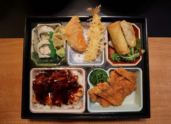 Japanese bento box with sushi rolls, shrimp and vegetable tempura, spring rolls, chicken katsu, seaweed salad, and teriyaki chicken over rice