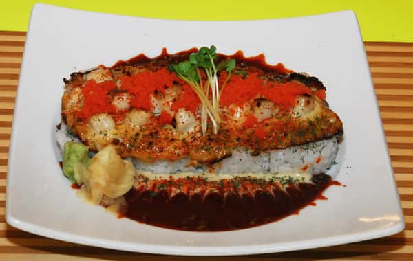 A sushi dish with scallops and spicy roe over rice, drizzled with dark sauce.