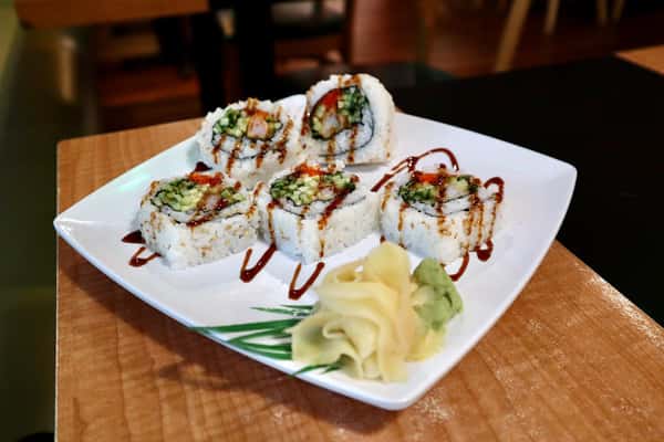 Plate of sushi rolls with avocado and cucumber, drizzled with sauce and served with wasabi and pickled ginger