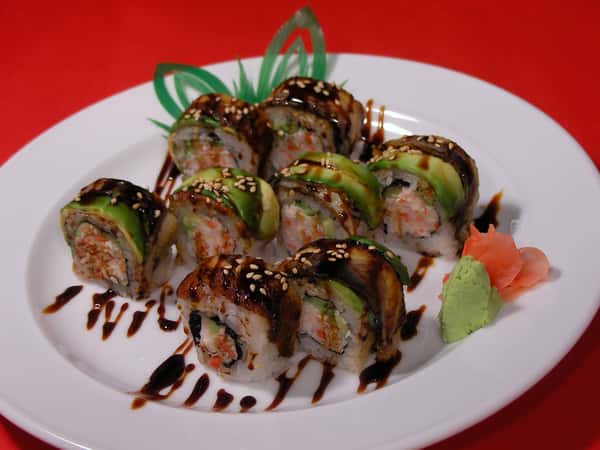 Sushi rolls topped with avocado and eel, drizzled with teriyaki sauce and sprinkled with sesame seeds.