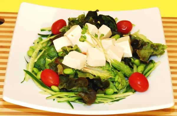A tofu salad is served on a mix of greens with cherry tomatoes and shredded vegetables.