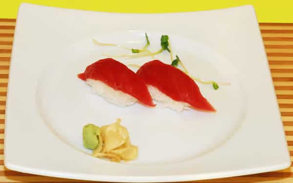 Two pieces of tuna nigiri with wasabi and ginger.