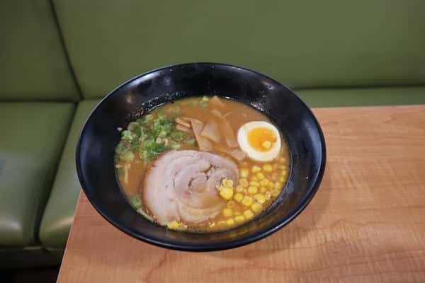 Bowl of ramen with sliced pork, corn, bamboo shoots, green onions, and a soft-boiled egg in broth