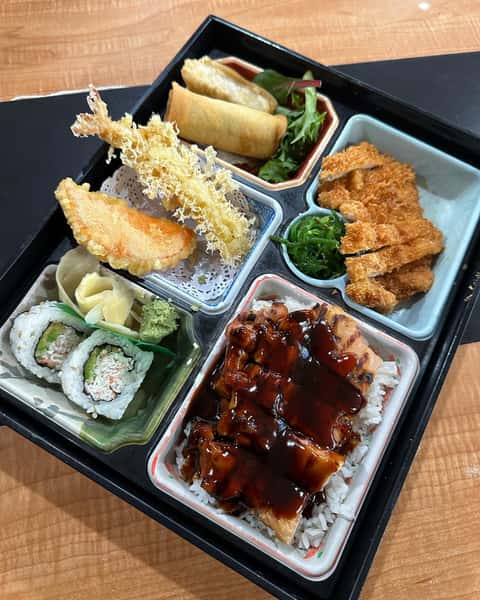 Japanese bento box with sushi rolls, shrimp and vegetable tempura, spring rolls, chicken katsu, seaweed salad, and teriyaki chicken over rice