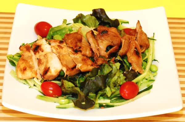 Grilled chicken served on a fresh green salad with cherry tomatoes and edamame.