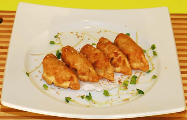 Fried dumplings are served neatly on a white plate with greens and sesame seeds.