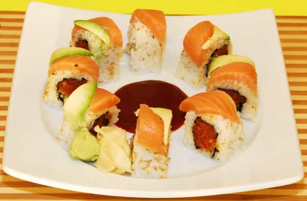 Sushi rolls with spicy filling, topped with salmon and avocado, arranged in a ring.