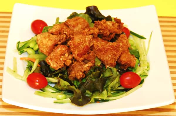 A crispy chicken salad is served on a bed of fresh greens with cherry tomatoes.