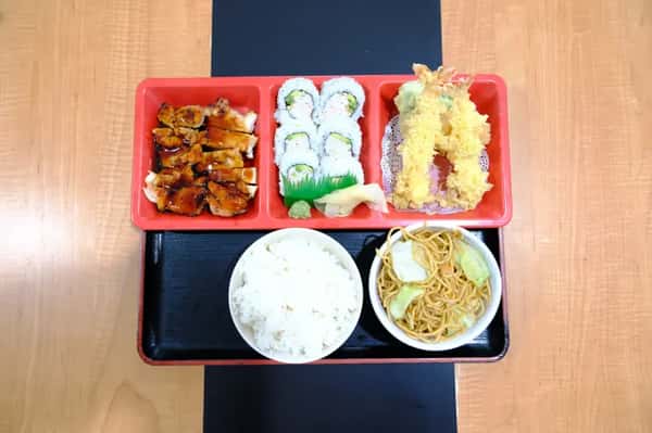 Japanese bento box with chicken teriyaki, sushi rolls, tempura, rice, and noodles