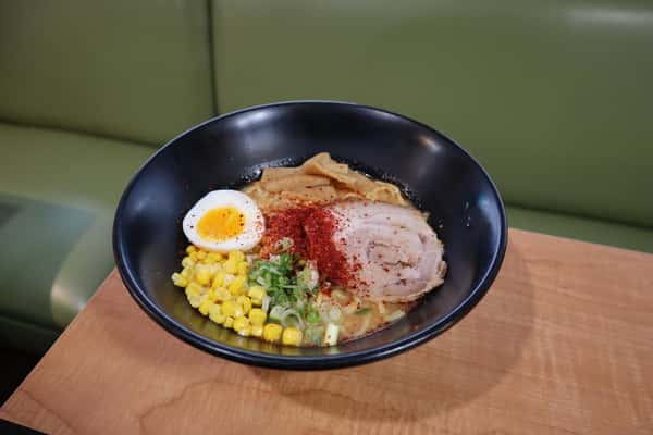 Bowl of ramen with sliced pork, corn, soft-boiled egg, bamboo shoots, green onions, and chili powder