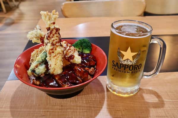 Bowl of teriyaki chicken with tempura and vegetables, served with a glass of Sapporo beer