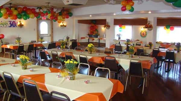 Private room for special events decorated with colorful balloons and tables set with orange and yellow linen with flower center pieces