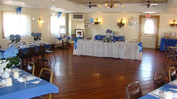 Main table in the center of a private hall set for a special occasion with blue and white decorations