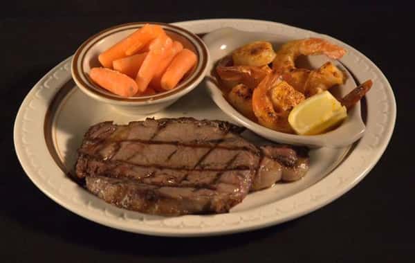 Grilled steak served with a side of fried shrimp with a lemon wedge and a side of baby carrots