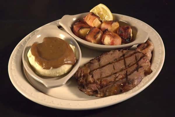 Grilled steak served with a side of bacon wrapped scallops and a side of mashed potatoes served with brown gravy