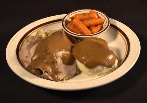 Roast beef dinner smothered with brown gravy and served with mashed potatoes and a side of roasted carrots