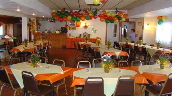 Private room for special events decorated with colorful balloons and tables set with orange and yellow linen with flower center pieces
