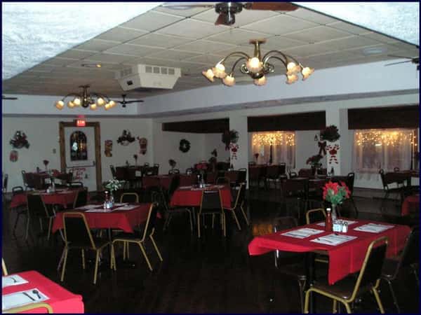 Dining hall set for dinner with tables covered in red linen with red roses in the center of the table tops