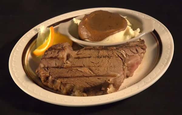 Steak served with mashed potatoes topped with brown gravy and orange slices on the side