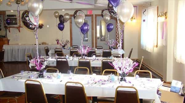 Private hall set for a special occasion with the tables decorated with white and purple balloons and flower centerpieces